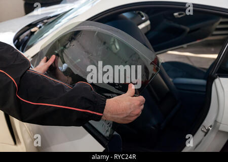 La procedura guidata per l'installazione di apparecchiature aggiuntive bastoni una tinta pellicola sul lato vetro anteriore della vettura e si appiattisce a mano per montare il vetro con una g Foto Stock