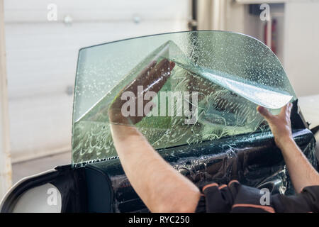 La procedura guidata per l'installazione di apparecchiature aggiuntive bastoni una tinta pellicola sul lato vetro anteriore della vettura e si appiattisce a mano per montare il vetro con una g Foto Stock