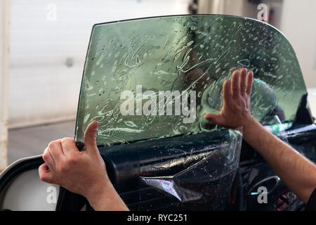 La procedura guidata per l'installazione di apparecchiature aggiuntive bastoni una tinta pellicola sul lato vetro anteriore della vettura e si appiattisce a mano per montare il vetro con una g Foto Stock