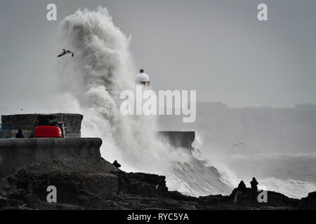 Onde enormi schiaffo contro la parete del porto come spettatori guarda dalle rocce in mezzo al mare a Porthcawl, in Galles, dove pioggia e forte vento hanno causato interruzioni di viaggi in diverse parti del Regno Unito come tempesta Gareth si sposta ad est. Foto Stock