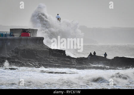 Onde enormi schiaffo contro la parete del porto come spettatori guarda dalle rocce in mezzo al mare a Porthcawl, in Galles, dove pioggia e forte vento hanno causato interruzioni di viaggi in diverse parti del Regno Unito come tempesta Gareth si sposta ad est. Foto Stock