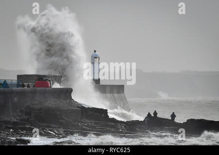 Onde enormi schiaffo contro la parete del porto come spettatori guarda dalle rocce in mezzo al mare a Porthcawl, in Galles, dove pioggia e forte vento hanno causato interruzioni di viaggi in diverse parti del Regno Unito come tempesta Gareth si sposta ad est. Foto Stock