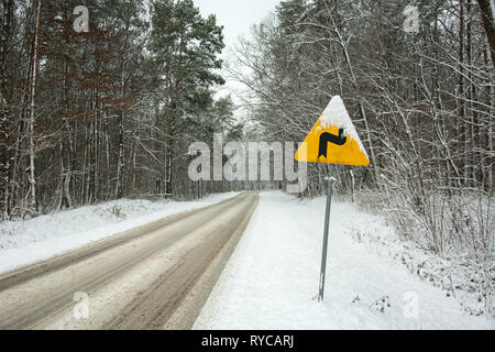 Avviso di colore giallo cartello stradale - curve pericolose, prima a destra - in piedi dalla strada attraverso la foresta - vista invernale Foto Stock