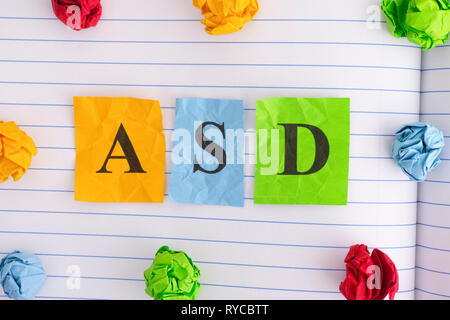 ASD. ASD (autismo disordine di spettro) sul foglio di notebook con alcuni colorata carta sgualcita sfere intorno ad esso. Close up. Foto Stock