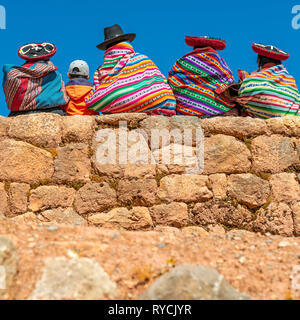 Fotografia quadrata di indigeni quechua dame in abiti tradizionali con un giovane ragazzo seduto su un muro Inca nella Valle Sacra degli Inca, Perù. Foto Stock