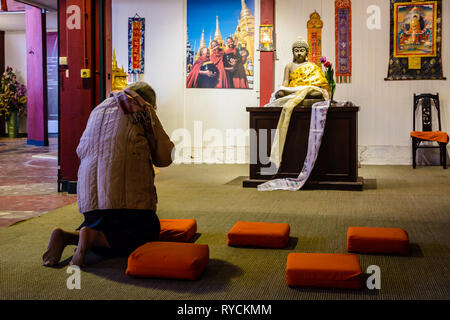 Una vecchia donna in ginocchio prega davanti ad un piccolo altare con una statua del Buddha in una camera separata nella Grande Pagoda di Vincennes a Parigi, Francia. Foto Stock