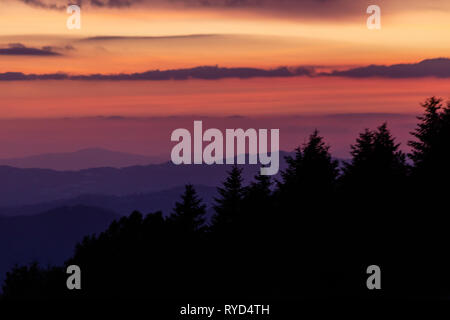 Alberi sagome contro un colore bellissimo cielo al tramonto, con montagne di strati in background Foto Stock