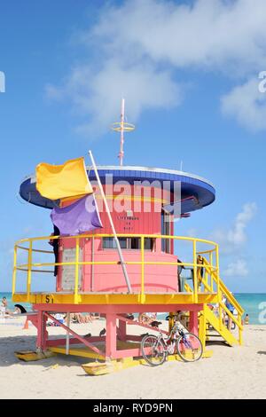 Colorfully dipinto Art Deco stazione bagnino sulla soleggiata spiaggia Sud con giallo e viola surf flag di avviso in caso di vento forte, Miami, Florida, Stati Uniti d'America Foto Stock