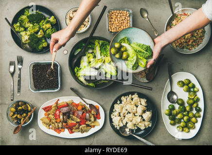 Cena vegana impostazione tabella. Piatti sani in piastre su tavola. Flat-lay di insalate di verdura, legumi, i fagioli, olive, germogli hummus e donna mani m Foto Stock