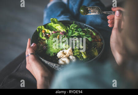 Un sano pranzo o cena a casa. Vegan superbowl Buddha o ciotola con hummus, verdure, insalate fresche, fagioli, couscous e avocado in mani femminili Foto Stock