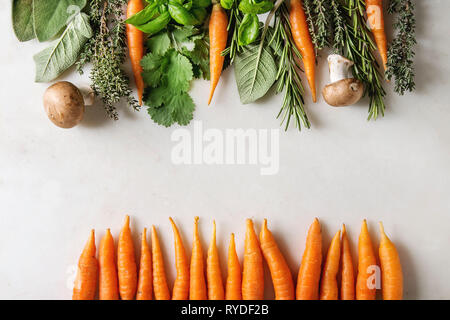 Varietà di cucina fresca erbe con mini carote e funghi champignon in fila su marmo bianco dello sfondo. Appartamento laico, spazio. Concetto di cucina a vista, cibo Foto Stock