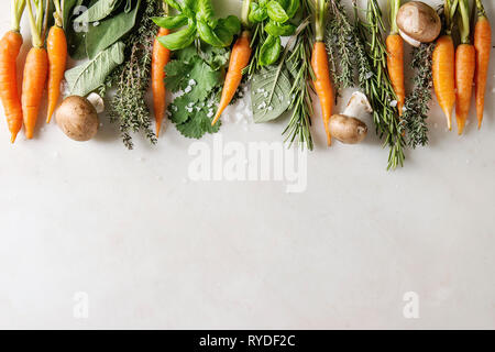 Varietà di cucina fresca erbe con mini carote e funghi champignon in fila su marmo bianco dello sfondo. Appartamento laico, spazio. Concetto di cucina a vista, cibo Foto Stock