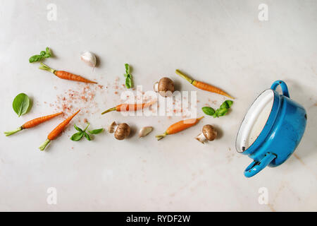 Il basilico fresco erbe con mini carote, sale e funghi champignon levitazione nella coppa blu su bianco Sfondo marmo. Appartamento laico, spazio. La cottura con Foto Stock