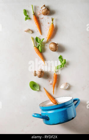 Il basilico fresco erbe con mini carote, sale e funghi champignon levitazione nella coppa blu su bianco Sfondo marmo. Appartamento laico, spazio. La cottura con Foto Stock