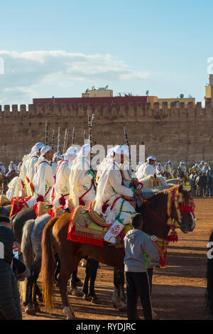 Meknes, Marocco - Marzo 31, 2018: uniformata gruppo tribale con fucili montati su cavalli in attesa di Tbourida Fantasia vicino a Medina parete in Meknes, Moroc Foto Stock