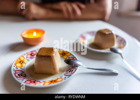 Dolce panna cotta piatti da dessert con candela accesa sul tavolo e cucchiai e uomo seduto in sfondo bokeh di fondo in ambienti interni in Italia illuminata data romantico Foto Stock