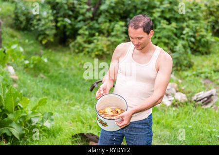 Giovane agricoltore in giardino sporco di risciacquo da homegrown lavare le patate in una pentola di cottura estate verde in una fattoria fuori Foto Stock