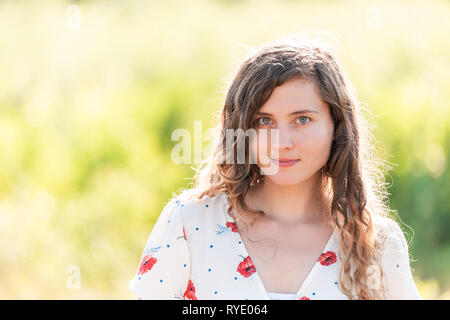 Ritratto di giovane volto di donna sorridente felice closeup nella soleggiata estate giallo verde parco al tramonto con lunghi capelli ondulati e sfondo bokeh di fondo Foto Stock