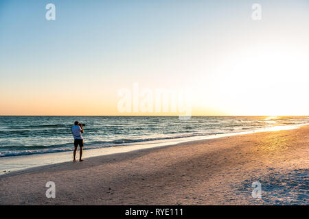 Giovane fotografo professionista sta immagine foto del tramonto sulla spiaggia in Florida Siesta Key da Sarasota da spiaggia onde tengono grande fotocamera Foto Stock
