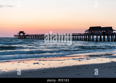 Naples, Florida e Rosa pastello Giallo crepuscolo al tramonto nel golfo del Messico con Pier e colonne di legno su orizzonte con blu scuro oceano onde di marea e Foto Stock
