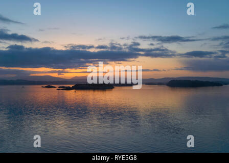 Dawn inizio a rompere su isole nel fiordo di Bergen su una calma gli inverni di mattina con increspature giocando attraverso la superficie dell'acqua. La Norvegia. Foto Stock