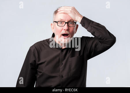 Senior Uomo in camicia nera mettendo la sua mano sulla fronte di ricordare qualcosa Foto Stock