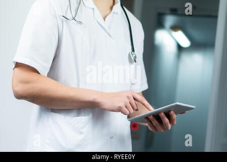 Luminose ravvicinata di un medico di sesso maschile in uniforme con uno stetoscopio e utilizzando computer tablet in ospedale. Moderno concetto medico Foto Stock