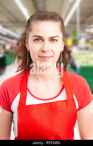 Ritratto di donna ipermercato o dipendente del supermercato con gravi sorriso e capelli legati a coda di cavallo indossando grembiule rosso Foto Stock