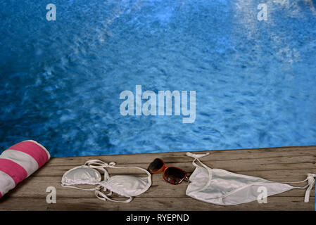 Donna sinistra asciugamano e bikini su pavimento in legno in piscina piscina Foto Stock
