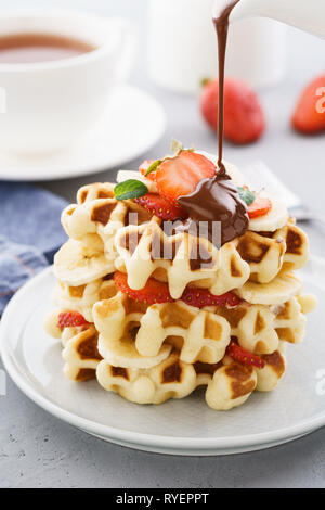 Pila di waffles fatti in casa con banana, fragola e fluente cioccolato. Foto Stock