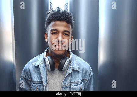 Per il tempo libero all'aria aperta. Mulatto guy con cuffie attorno al collo in piedi su una strada di città guardando la telecamera fiducioso close-up Foto Stock