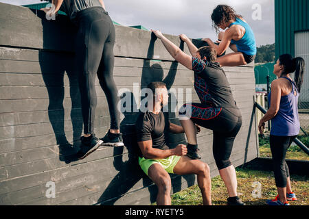 I partecipanti nel corso di ostacolo parete di arrampicata Foto Stock