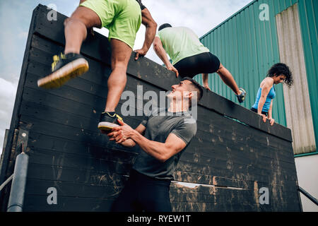 I partecipanti nel corso di ostacolo parete di arrampicata Foto Stock