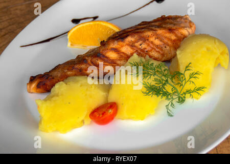 Filetto di salmone alla griglia con purè di patate. E levetta di aneto, pomodoro ciliegino, un pezzo di limone e salsa di melograno. Primo piano. Foto Stock