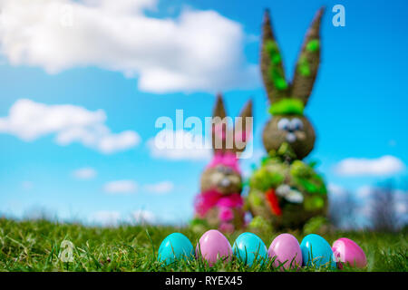 La paglia figura Bunny con colorate Uova di Pasqua grassand verde blu del cielo la Pasqua e la molla dello sfondo. blur Foto Stock