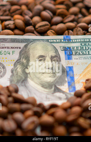 Banconota da 100 dollari americani, tra i chicchi di caffè. Il concetto di business per l'acquisto, la vendita, la fornitura e distribuzione di caffè. Foto Stock