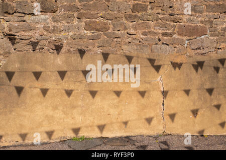 Il sole luminoso crea ombre di bunting appeso tettuccio di creare un modello di un sbriciolare un muro di mattoni. Foto Stock