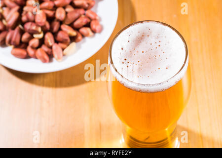 Un bicchiere di schiumosa, birra schiumosa e noccioline nel piattino. Foto Stock