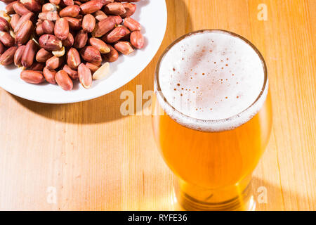 Un bicchiere di schiumosa, birra schiumosa e noccioline nel piattino. Foto Stock