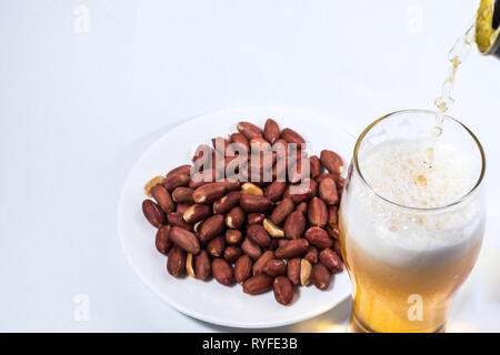 La birra viene versata in un bicchiere e noccioline nel piattino. Foto Stock