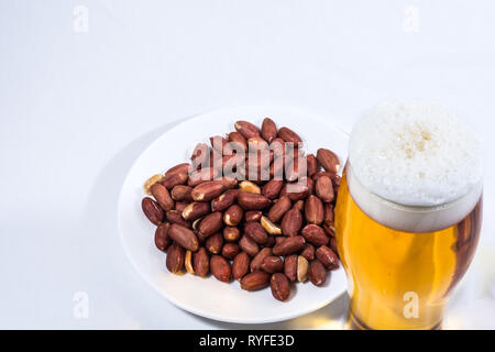 Un bicchiere di schiumosa, birra schiumosa e noccioline nel piattino. Foto Stock