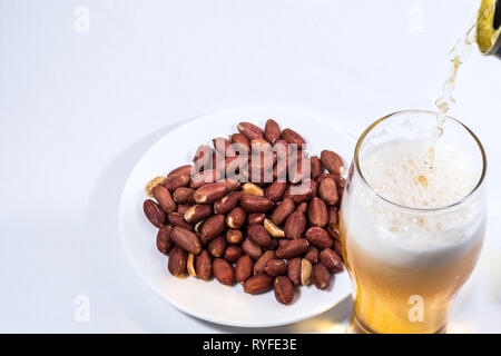 La birra viene versata in un bicchiere e noccioline nel piattino. Foto Stock