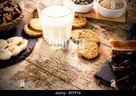 Tavolo in legno impostato per un dolce vegan prima colazione con la bevanda di riso, fette di banana, frutta secca mista, vegan biscotti, fette di pane con marmellata e crema di Foto Stock