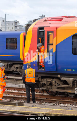 Clapham Junction, Londra, Regno Unito; 13 marzo 2019; Macchinista si appoggia al di fuori della cabina. Colloqui con due colleghi. Tutti arancione di usura ad alta visibilità indumenti di sicurezza Foto Stock