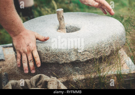 L'antica pietra quern mulino a mano con grano. L'uomo macina il grano in farina con l aiuto di una macina. Gli uomini con le mani in mano su una macina. Vecchio Foto Stock