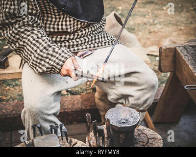 Il fabbro nel processo di produzione di prodotti in metallo a mano sull'openair di officina. Le mani di un fabbro con red hot billetta close up Foto Stock