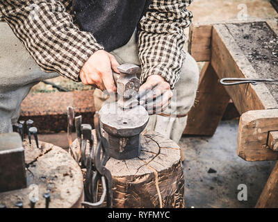 Mano fabbro con un martello sull'incudine di acciaio . La mano di un fabbro con un martello vicino. Il fabbro nel processo di produzione di prodotti in metallo Foto Stock