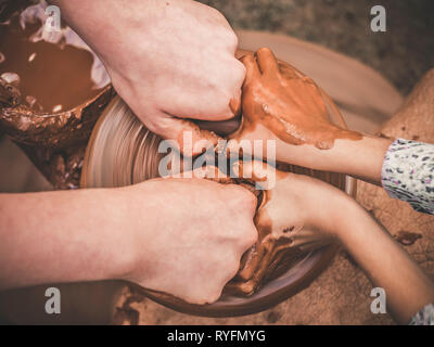 Insegnamento in ceramica un carftman le mani a guidare un bambino mano, mostrando come buttare una pentola di creta su una ruota di vasai. Insegnante e studente concetto. Vista superiore Foto Stock