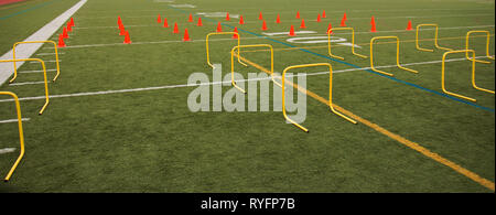Coni di arancione e giallo soglie sono impostate su un tappeto erboso verde campo per la pratica della velocità di alta scuola di sport. Foto Stock