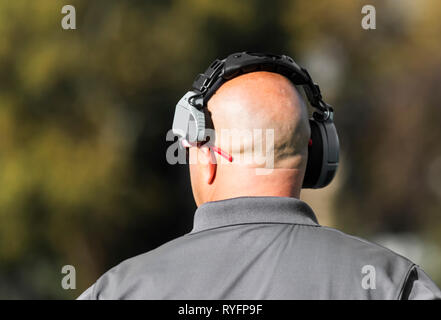 Una scuola di allenatore di calcio ha il suo auricolare mentre guardando verso il basso il campo di gioco essendo gestito dalla sua squadra. Foto Stock